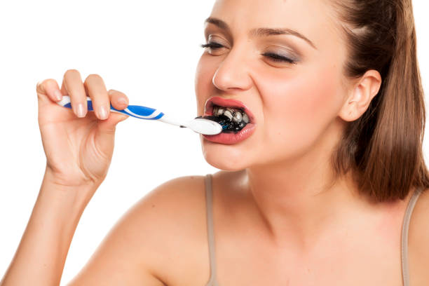 istock young woman brushing her teeth with black toothpaste of activated charcoal on white background 996616550