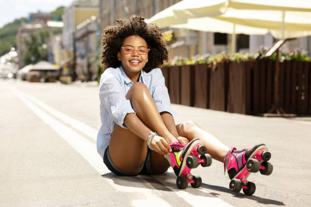 istock Cheerful curly girl smiling while putting on roller skates 996626768