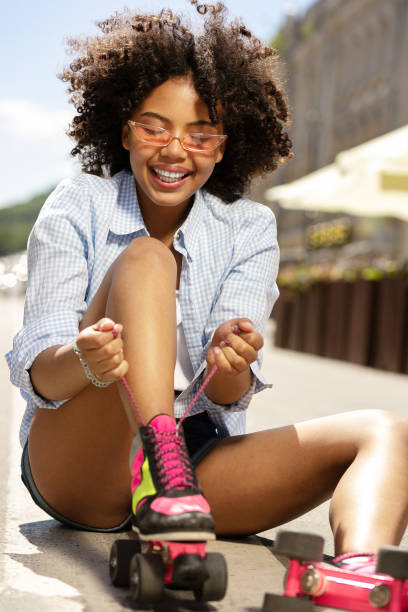 istock Upbeat curly girl smiling while tying roller skate laces 996626786