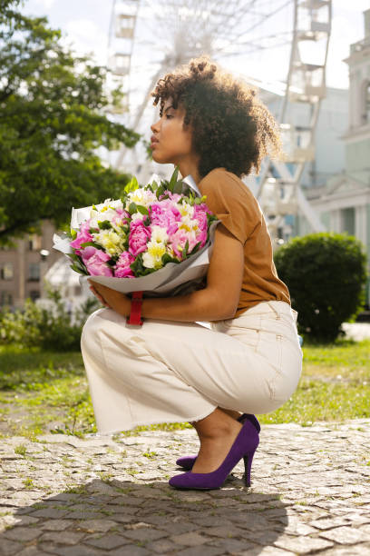 istock Slender curly woman holding bouquet and squatting 996627378