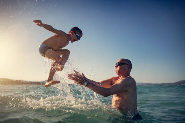 senior homme jouant avec petit-fils en mer - grands évènements de la vie photos et images de collection