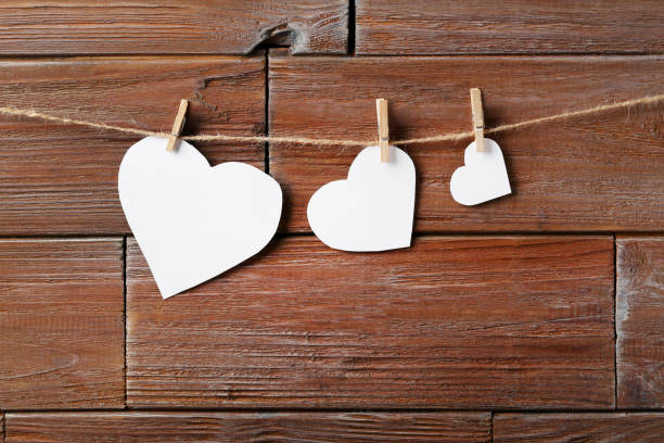istock White paper hearts hanging on wooden background 996714748