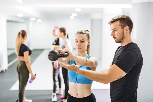 Assistance for the begginers in the gym - personal trainer assisting to the beautiful girl Young people - teenagers and young adults exercising on cross training with variety of exercises crossfit girl stock pictures, royalty-free photos & images