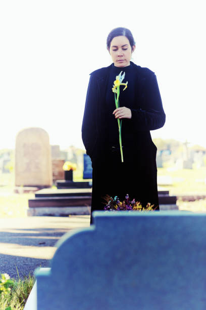 istock Young woman mourner carries single iris to grave 996733960