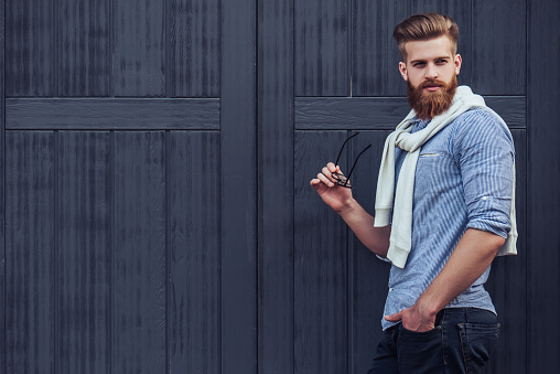 Stylish bearded man is posing on black wooden background in the city. Young man with eye glasses isolated.