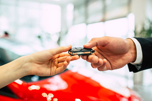 The car seller in the dealership passes the keys to the young woman. Handing of car keys. The car seller in the dealership passes the keys to the young woman. car key photos stock pictures, royalty-free photos & images