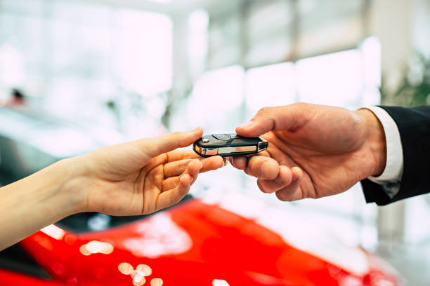 the car seller in the dealership passes the keys to the young woman. - chave de carro imagens e fotografias de stock