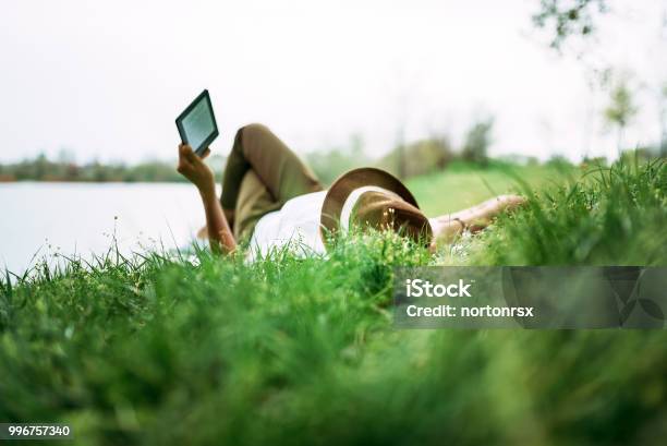 Enjoying Ebook Near The Lake Girl Lying In The Grass Stock Photo - Download Image Now