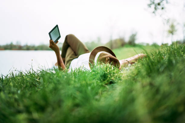 korzystanie z e-book w pobliżu jeziora. dziewczyna leży w trawie. - kindle e reader book reading zdjęcia i obrazy z banku zdjęć