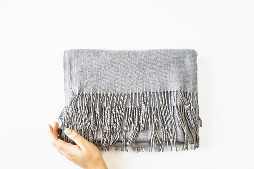 Gray cashmere female scarf folded in a rectangle with female hands on a white background. Minimalism. Top view, flat lay