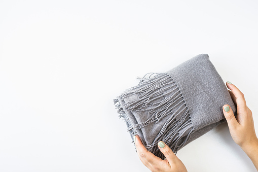 Gray cashmere female scarf folded in a rectangle with female hands on a white background. Minimalism. Top view, flat lay