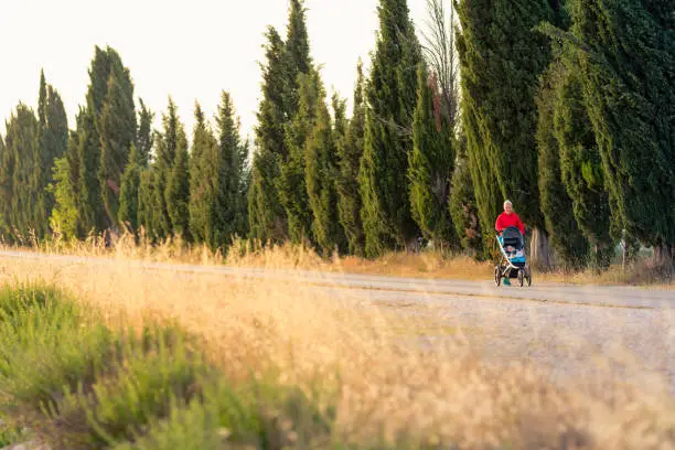 Running super mother with child in baby stroller enjoying sunset and mountains landscape. Jogging or power walking supermom, active family at sunset. Beautiful inspirational mountains landscape.