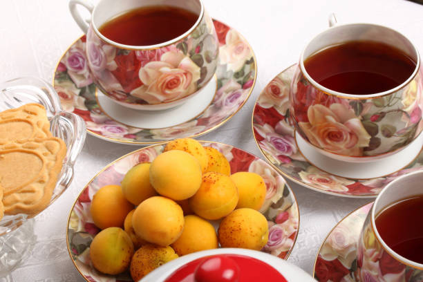 istock Porcelain teacups with hot tea and with floral pattern, teapot, biscuits and plate with wild apricots on a table 996769378