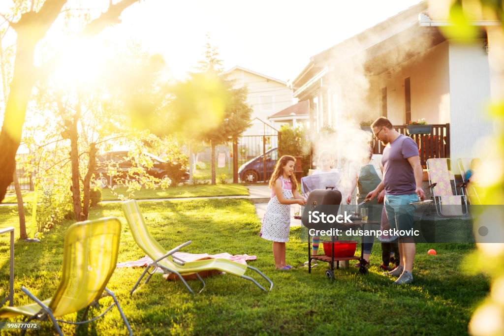 Hermosa pareja y sus hijos adorables se han reunido alrededor de la parrilla delante de la casa. - Foto de stock de Barbacoa - Comida libre de derechos