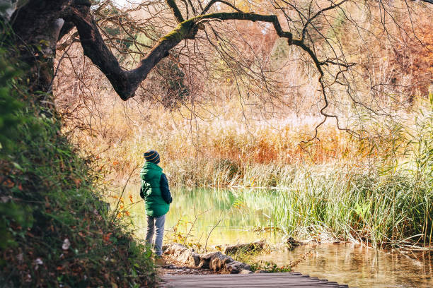 istock Boy stay  under big tree near the pond in autumn park 996781070