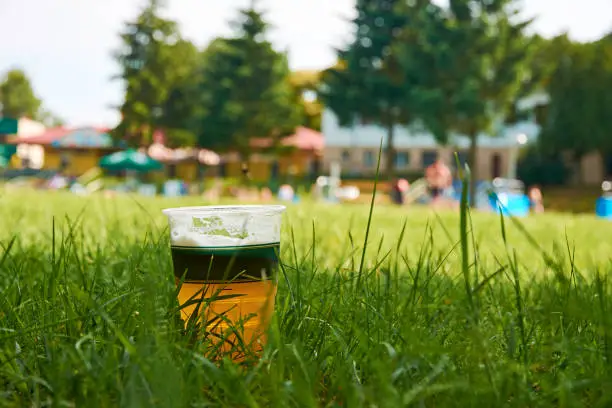 Crucible of beer standing in the grass by the pool with blurred trees and buildings in the background on a sunny summer day