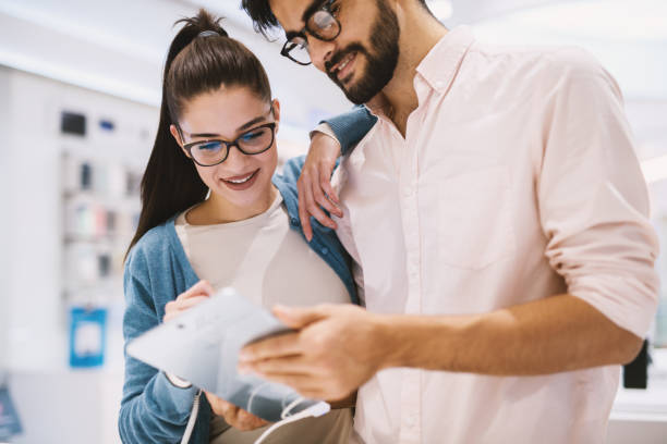 istock Cute young couple is checking out a test tablet in a bright tech store. 996787196