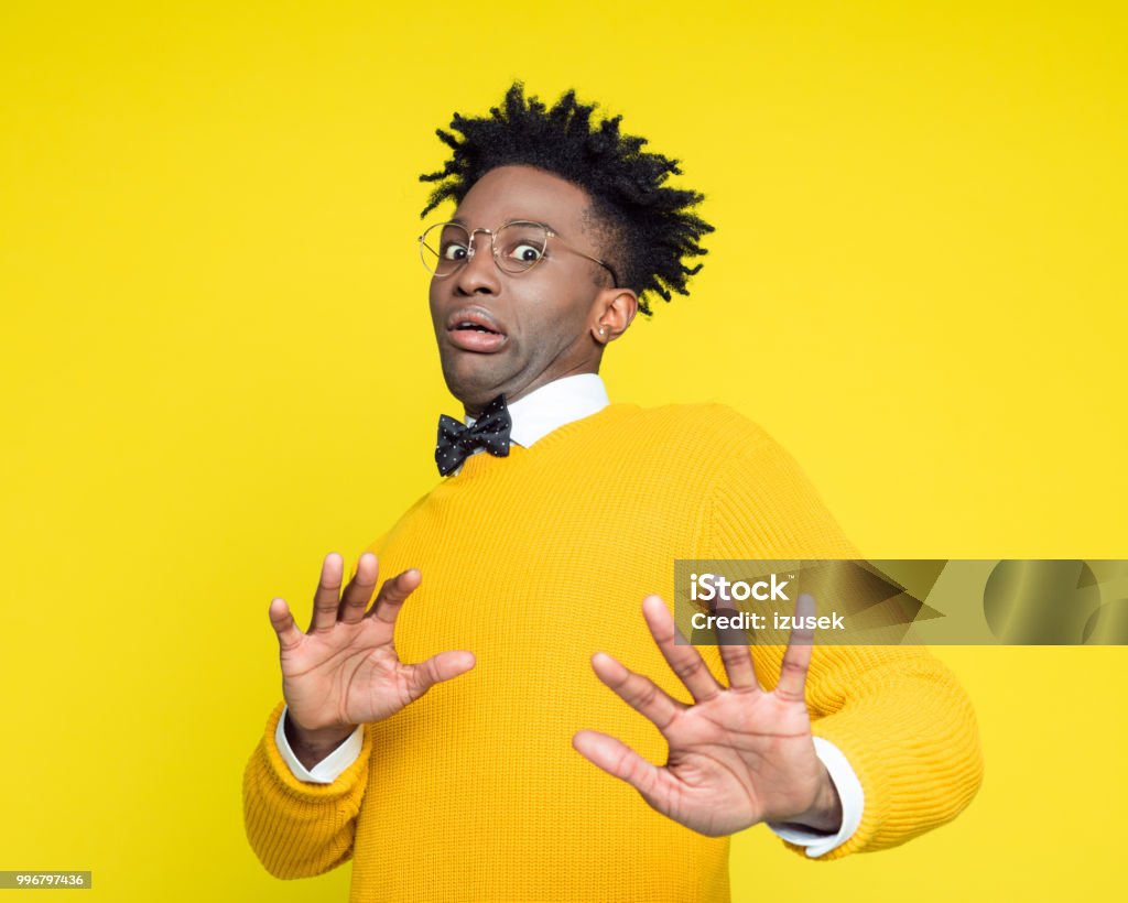 Portrait of worried geeky young man in retro style Funny portrait of worried nerdy young afro American man wearing yellow sweater and black bow. Studio shot against yellow background. Humor Stock Photo