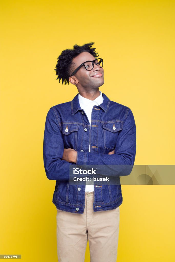 80's style portrait of happy geeky young man Portrait of happy nerdy young afro American man wearing oversized jeans jacket and glasses, standing against yellow background. Portrait Stock Photo