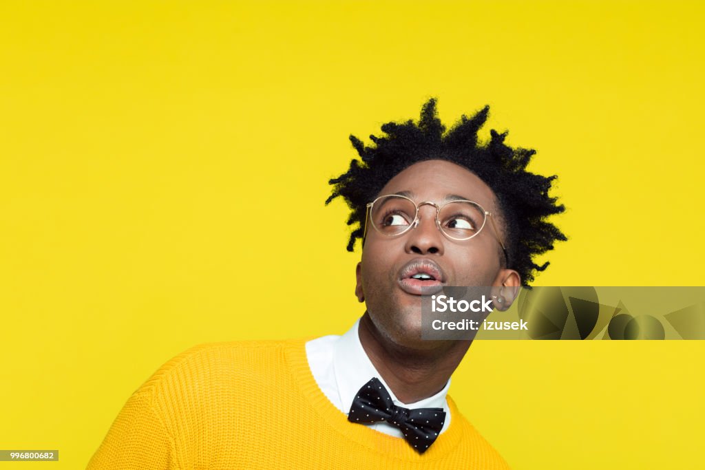 Funny portrait of surprised nerdy young man looking up Funny portrait of surprised cheesy nerdy young afro American man wearing yellow sweater, black bow tie and glasses, looking up. Men Stock Photo