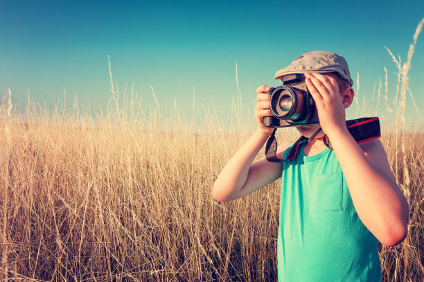A teenager boy looks through the lens of a camera against the background of a wall and takes pictures