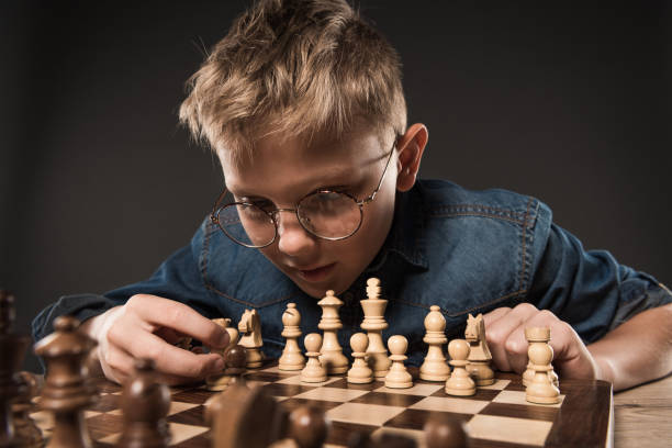 istock focused little boy in eyeglasses playing chess at table isolated on grey background 996807804