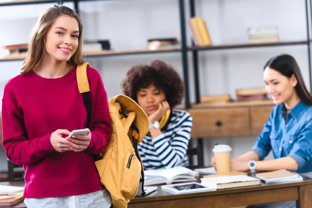 istock selective focus of smiling student with smartphone and multicultural friends studying behind 996812392