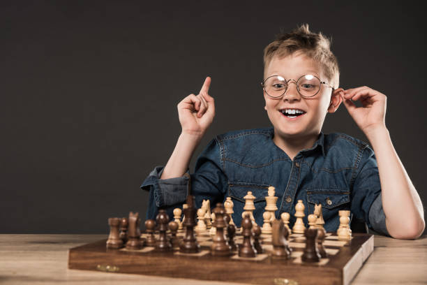 istock happy little boy in eyeglasses doing idea gesture by finger at table with chess board isolated on grey background 996812762