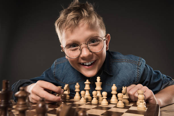 istock smiling little boy in eyeglasses playing chess isolated on grey background 996812888