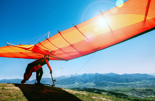 Man with hang-glider starting to fly from the hill top