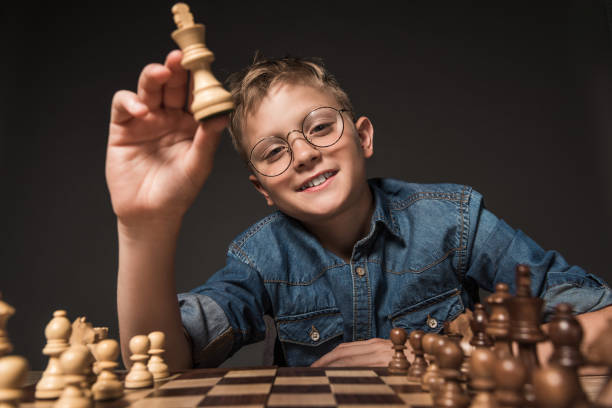 istock smiling little boy in eyeglasses holding chess figure over chessboard isolated on grey background 996822410