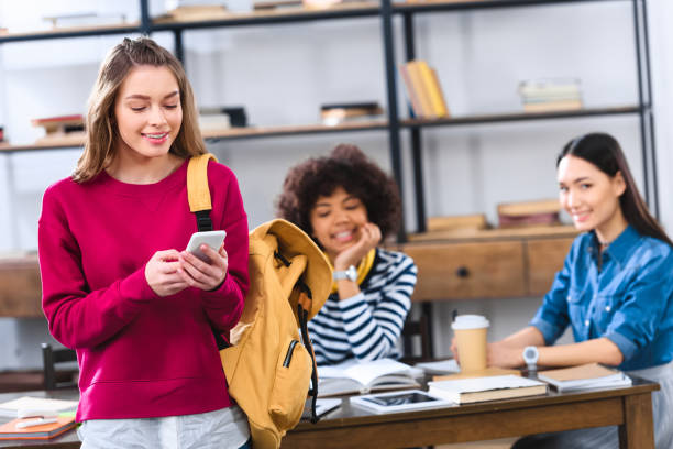 istock selective focus of smiling student with smartphone and multicultural friends studying behind 996824726