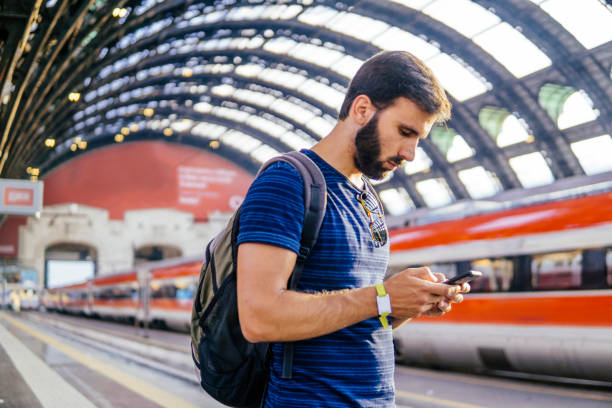 istock Beautiful young man looking at the phone while waiting for the train 996828518