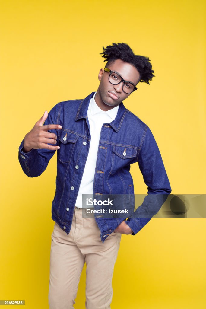 80's style portrait of confident nerdy young man Portrait of nerdy young afro American man wearing oversized jeans jacket and glasses, standing against yellow background. 1980-1989 Stock Photo