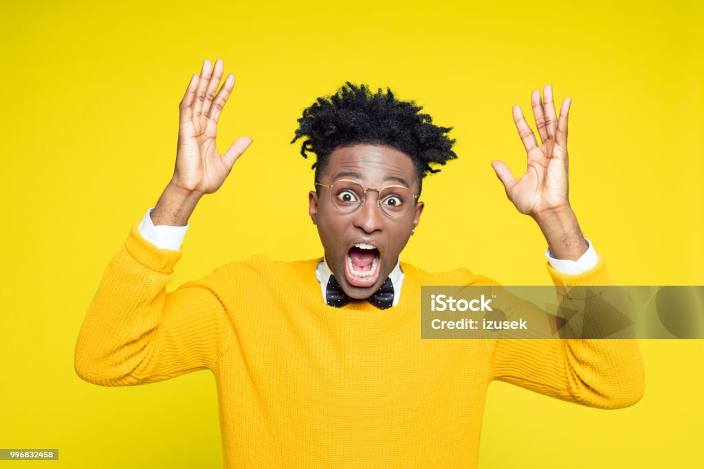 Portrait of angry nerdy young man gesturing against yellow background Portrait of angry nerdy young afro american man wearing yellow sweater and black bow tie gesturing against yellow background. Nerd Stock Photo