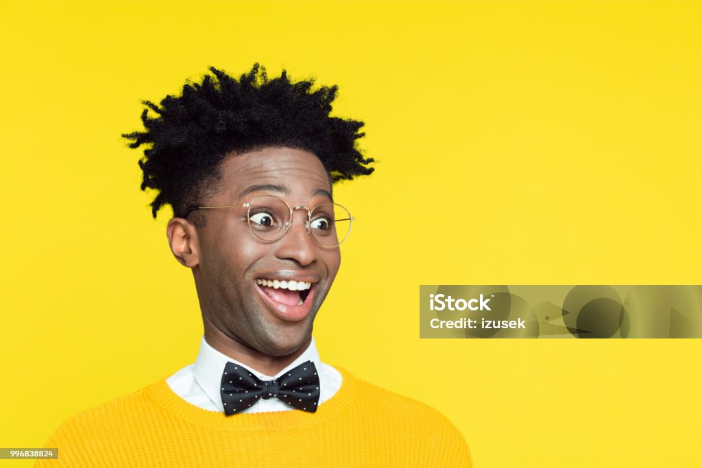 Funny portrait of surprised geeky young man Funny portrait of surprised nerdy young afro American man wearing yellow sweater and black glasses, standing against yellow background. Comedian Stock Photo