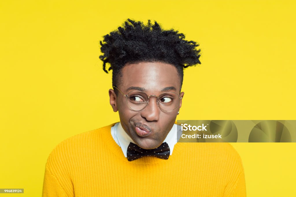 Funny portrait of nerdy young man making decision Funny portrait of pensive nerdy young afro American man wearing yellow sweater, black bow tie and glasses, making a decision. Asking Stock Photo