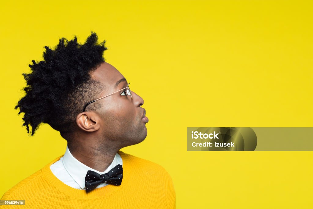Side view of nerdy young man looking at copy space Side view of nerdy young afro american man wearing yellow sweater and black bow tie looking at copy space against yellow background. Surprise Stock Photo