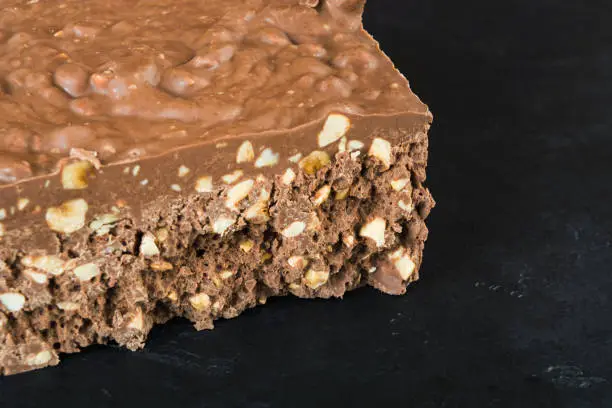 A big bar of milk chocolate with nuts and airbubbles over black background