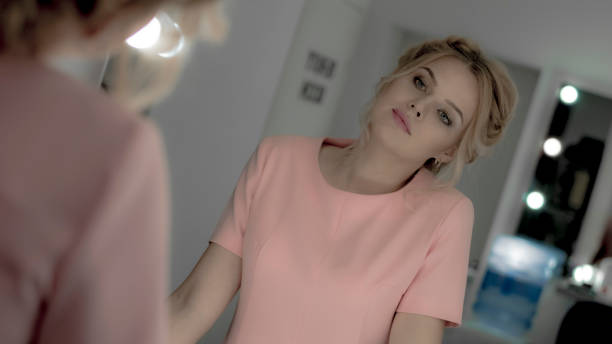 istock Charming young blonde with professional makeup and hairstyle look at mirror 996855586