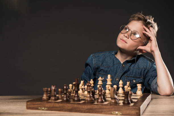 istock thoughtful little boy in eyeglasses sitting at table with chess board on grey background 996895340