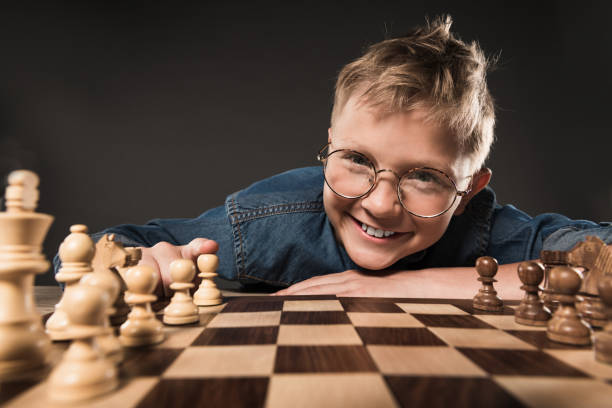 istock smiling little boy in eyeglasses looking at camera while sitting at table with chess board isolated on grey background 996899264