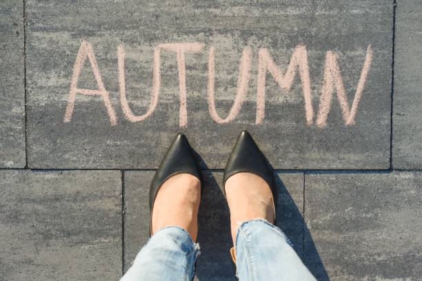 istock Female feet with text autumn written on grey sidewalk. 996904724