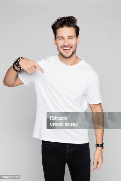Smiling Young Man Pointing Down Stock Photo - Download Image Now - T-Shirt, Men, White Color