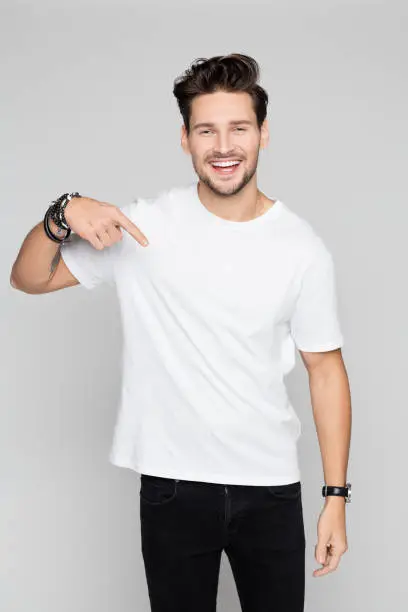 Portrait of young man pointing down and smiling on grey background