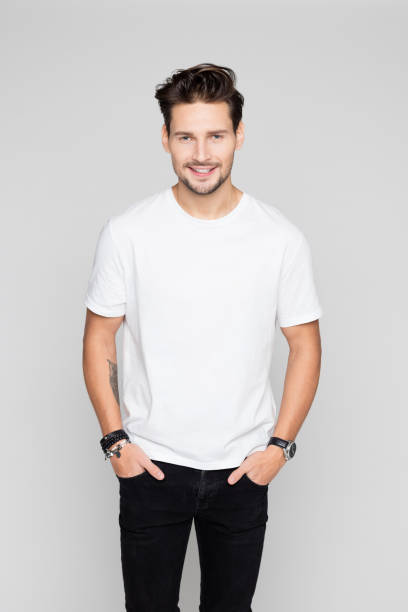 Portrait of handsome young man standing with his hands in pocket and looking at camera on grey background