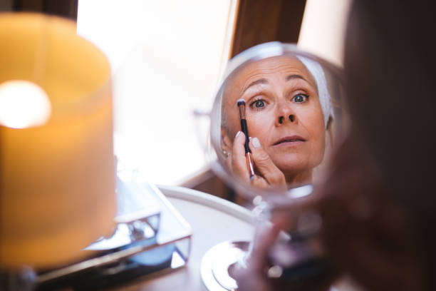 istock Mirror reflection view of mature woman applying make-up on face 996928884