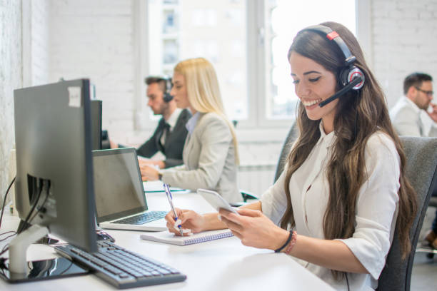 istock Beautiful business woman call operator with headset using mobile phone and writing notes to notebook at office desk 996934818