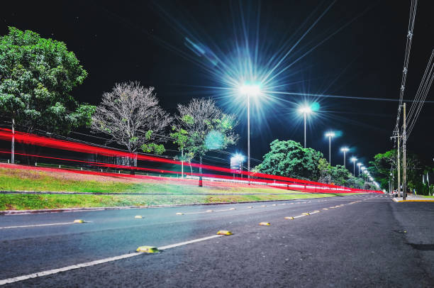 View of a city street surrounded by light poles and trees at night. stock photo