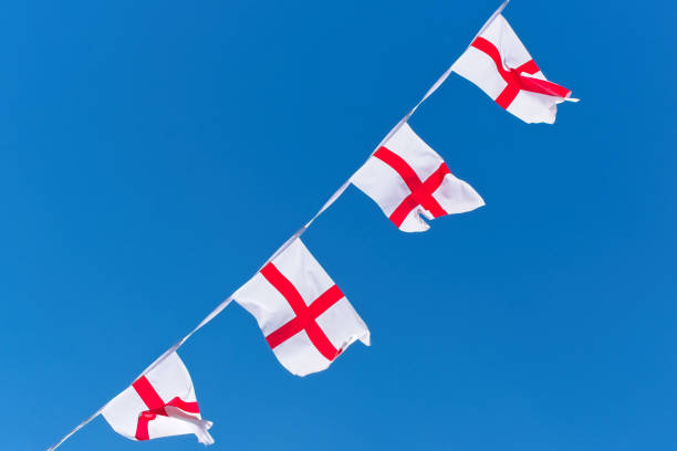 istock Single row of England flags / bunting flying against blue sky. 996965938
